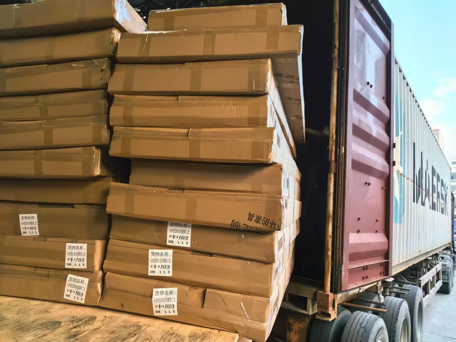 Cartons of packed cabinet panels stacked beside a shipping container during loading