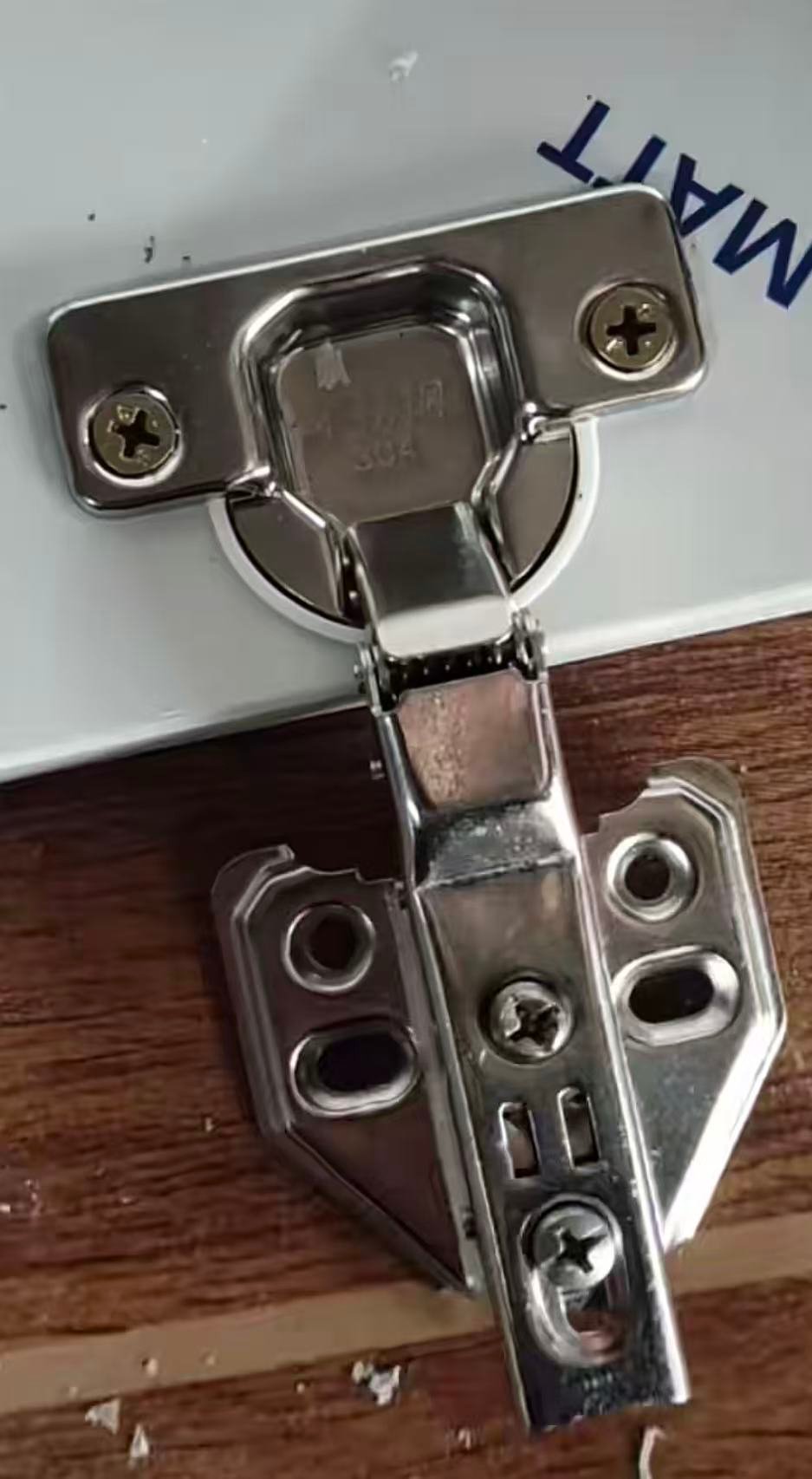 Concealed hinge screwed to a white cabinet door with its mounting plate on the cabinet side